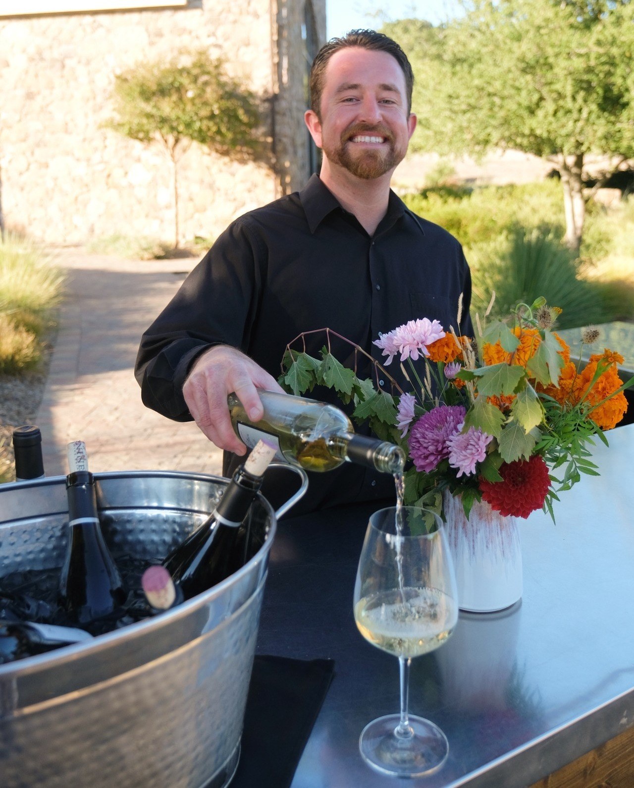 Matt Mesick Pouring a bottle of wine and smiling.