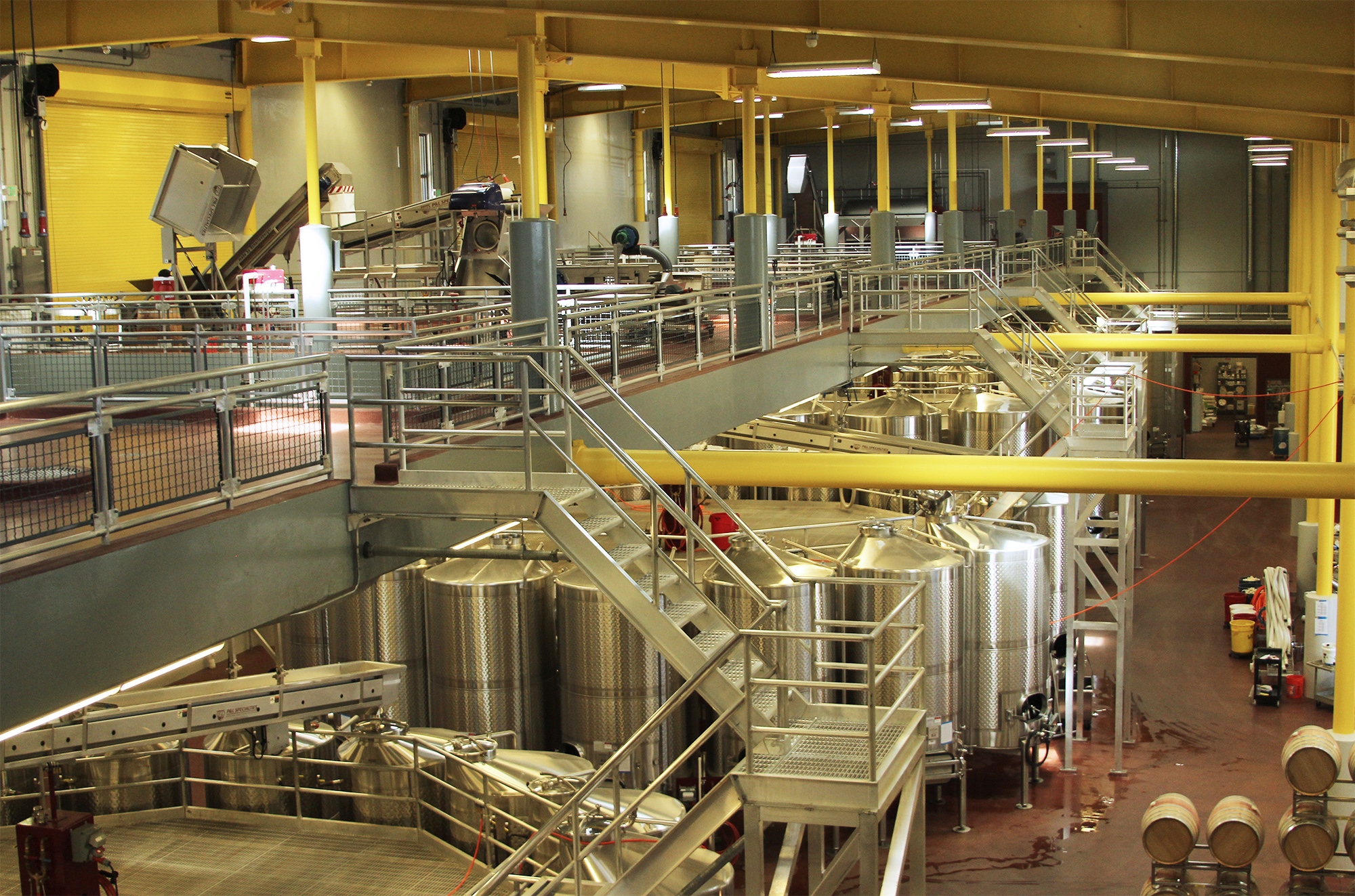 A shot of a winery, with stainless steel equipment and bright yellow support beams.