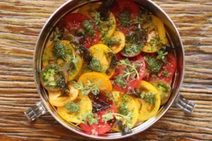 Red and yellow tomato salad in a stainles steel dish on top of a rough wooden table.