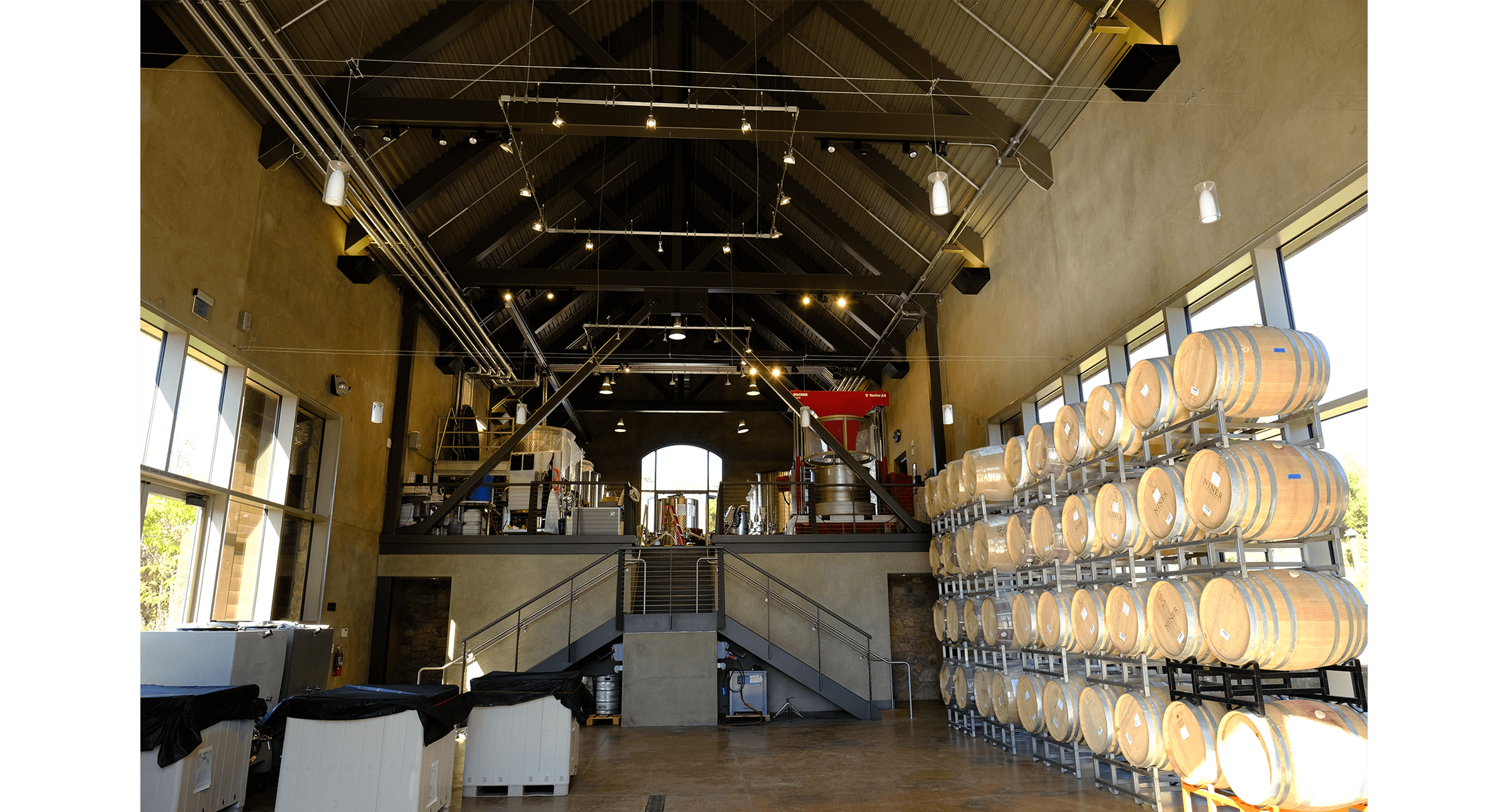 A winery is shown with fermenting tanks on one side and a stack of wine barrels on the other.