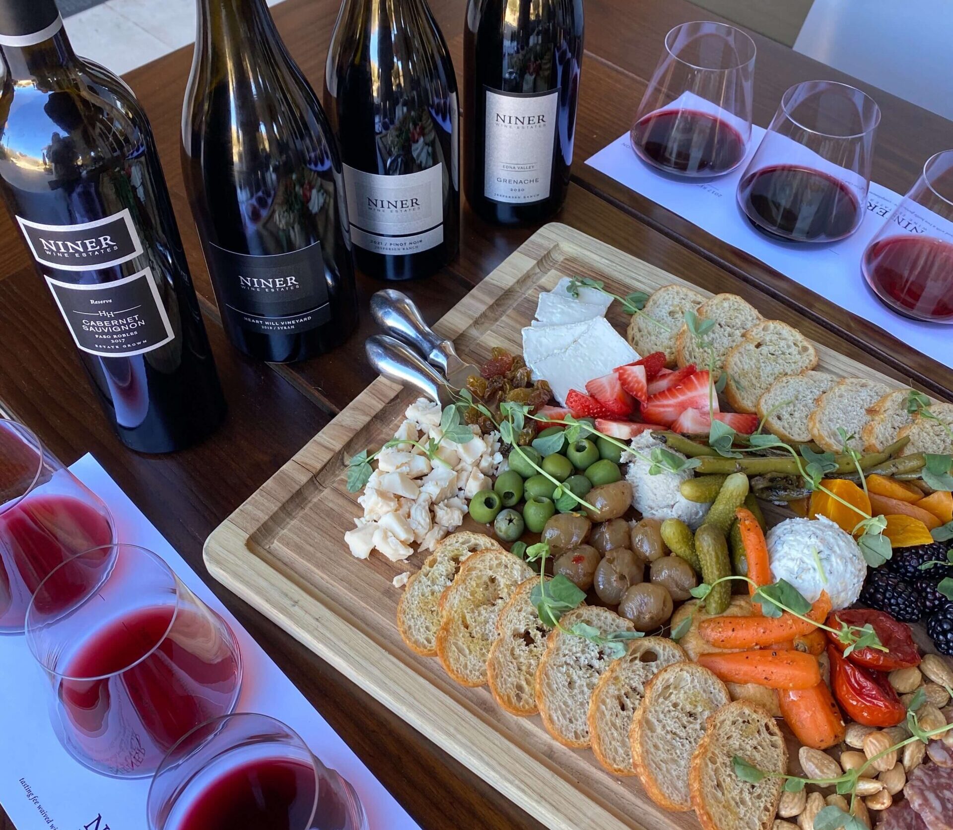 A cheese and charcuterie board alongside a tasting Flight of wine and bottles